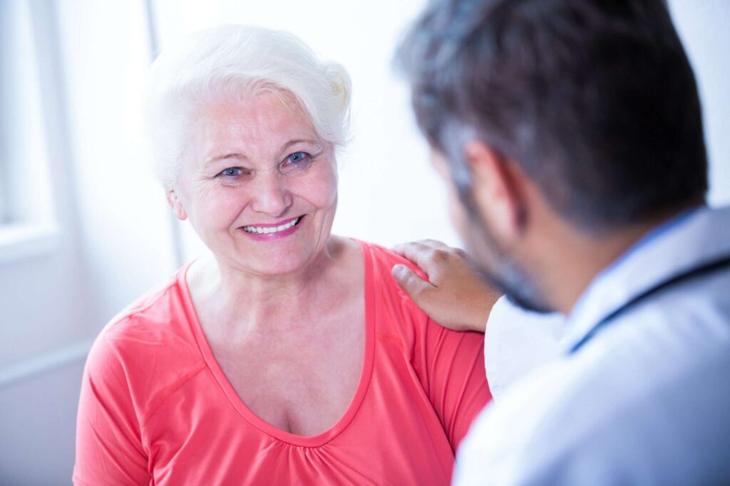 Smiling older woman with a carer's hand on her shoulder