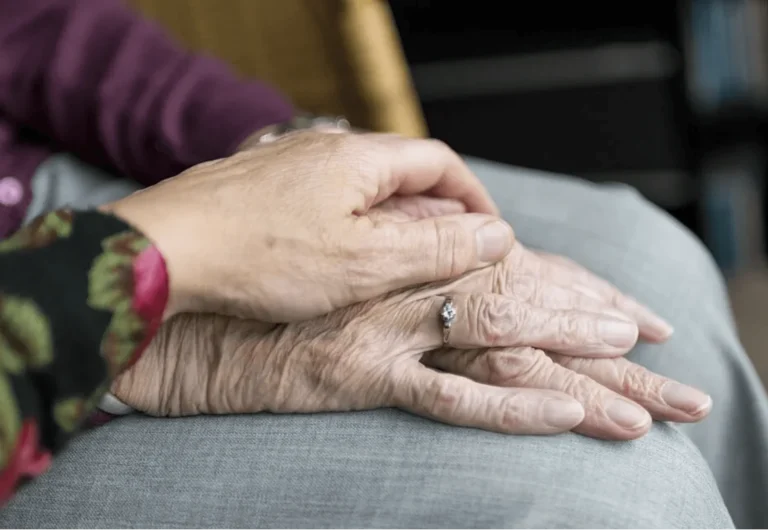 Carer's hand resting gently on an older person's hands