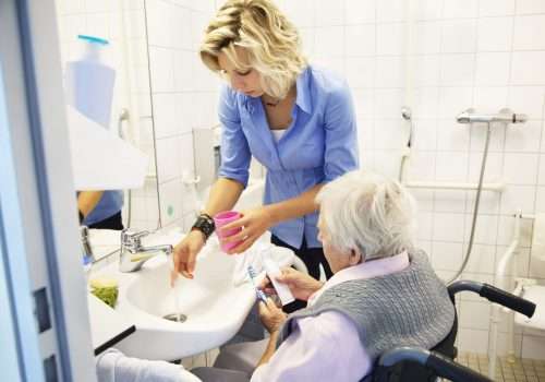 Carer helping an older woman wash at the sink