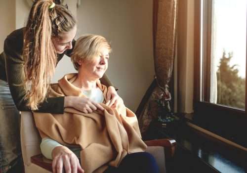 Carer comforting an older woman wrapped in a blanket